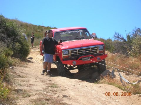 1985 Ford Bronco - A man stands by a red Ford Bronco as it navigates a rocky off-road trail.