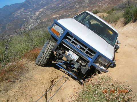 1985 Ford Bronco - Ford Bronco navigating a challenging off-road trail, showing its front 3/4 view.