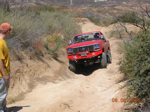 1985 Ford Bronco - Red Ford Bronco navigates a steep dirt trail with a person watching.