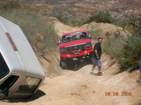 1985 Ford Bronco - Two off-road vehicles are stuck on a steep dirt trail, one being winched by the other.