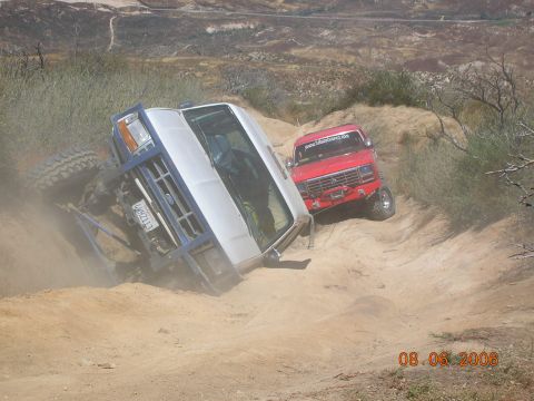 1985 Ford Bronco - Two off-road vehicles navigate a challenging dirt trail, with one vehicle overturned on its side.