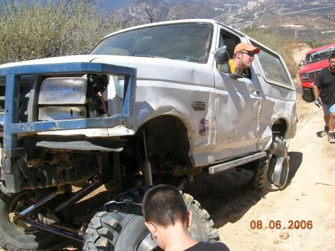 1985 Ford Bronco - A heavily modified white Ford Bronco is shown on a dusty trail with a man in the driver's seat.