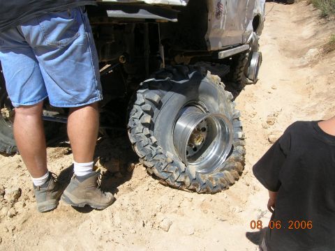 1985 Ford Bronco - A person stands next to an off-road vehicle with a severely damaged tire and rim on a dusty trail.