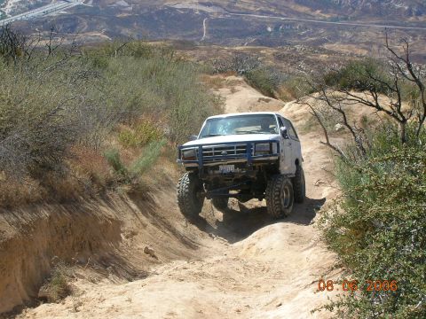 1985 Ford Bronco - This modified SUV navigates a steep dirt path in a dry, hilly landscape.
