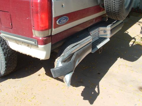 1990 Ford Bronco - The rear bumper of a Ford truck shows significant damage, with the spare tire mounted above.