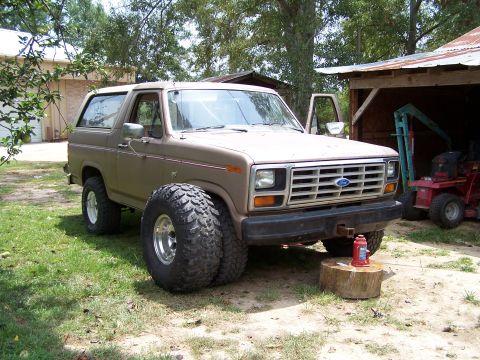 1981 Ford Bronco - A brown Ford Bronco is parked outside a barn, large off-road tires and a jack supporting the front bumper.