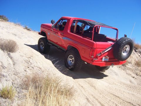 1985 Ford Bronco - A red Ford Bronco navigates a sandy incline under a clear blue sky.