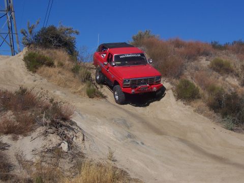 1985 Ford Bronco - Red Ford Bronco navigates a steep dirt trail under a clear blue sky.
