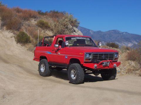 1985 Ford Bronco - This lifted 1985 Ford Bronco features an aftermarket bumper with a winch and is captured driving on a dusty trail.