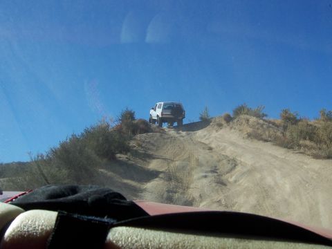 1985 Ford Bronco - A white SUV ascends a challenging dirt path under a clear blue sky.