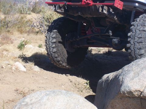 1985 Ford Bronco - The rear suspension and large tires of an off-road vehicle are visible as it traverses a rocky trail.
