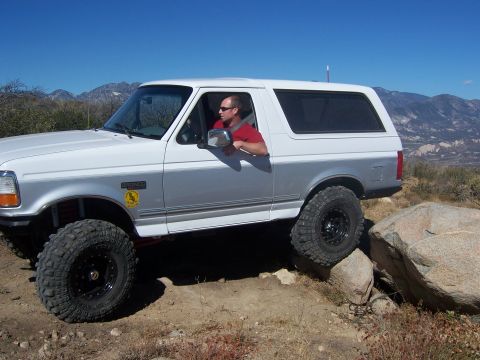 1985 Ford Bronco - This lifted Ford Bronco, likely a 1995 model, is shown navigating a rocky trail with its driver looking out the window.