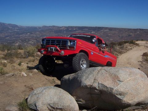 1985 Ford Bronco - Off-road Bronco navigating a challenging rocky path under a clear blue sky.