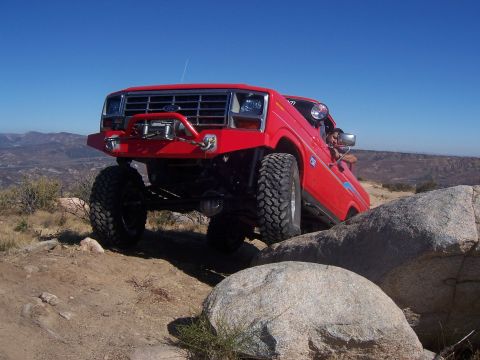 1985 Ford Bronco - This modified SUV navigates a rocky terrain under a clear blue sky.