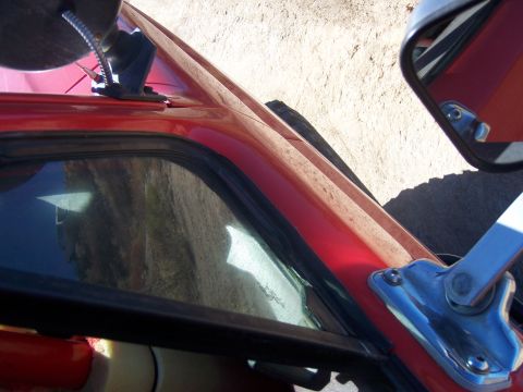 1985 Ford Bronco - Close-up of a red vehicle's door frame and window trim, showing exterior details.
