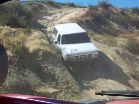 1985 Ford Bronco - A white SUV navigates a steep, dusty trail in a dry, hilly landscape.