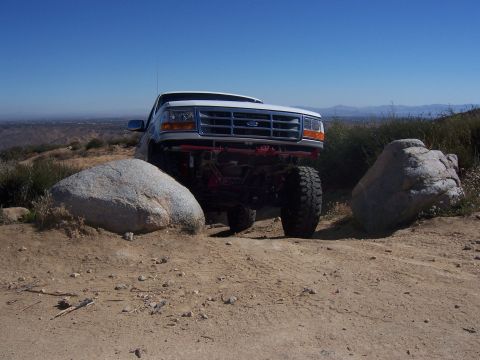 1985 Ford Bronco - A lifted Ford F-Series truck navigates a rocky trail under a clear blue sky.