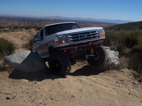 1985 Ford Bronco - This lifted Ford Bronco navigates a challenging off-road trail, demonstrating its off-road capabilities on a sunny day.