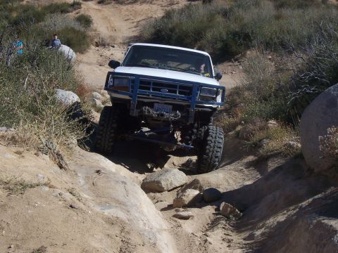 1985 Ford Bronco - This modified SUV navigates a challenging off-road trail, its front grille suggesting a 1987 model year.