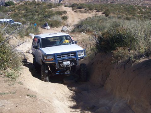 1985 Ford Bronco - A white Ford Bronco navigates a rocky off-road trail with a blue grille guard.