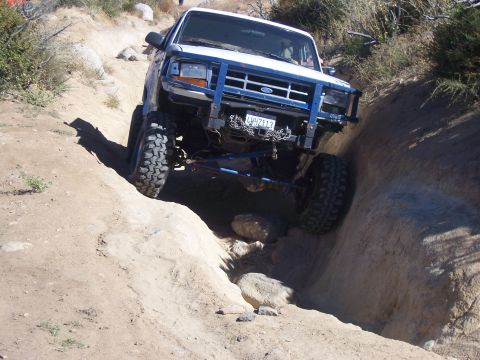 1985 Ford Bronco - This modified SUV navigates a challenging off-road course, its front tires climbing over rocks.
