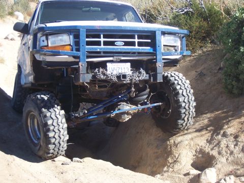 1985 Ford Bronco - This modified Ford truck navigates a challenging off-road terrain with its front end angled downwards.