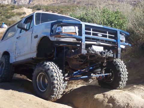 1985 Ford Bronco - This modified Ford Bronco, likely from the early 1990s, navigates a challenging off-road terrain.