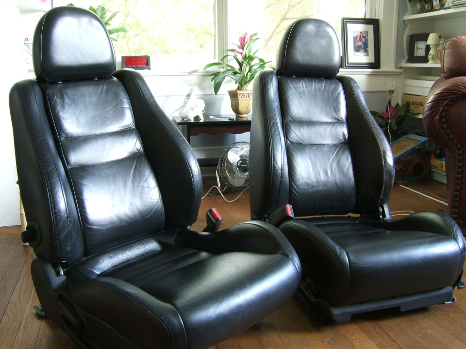 Two black leather car seats with headrests and seatbelts