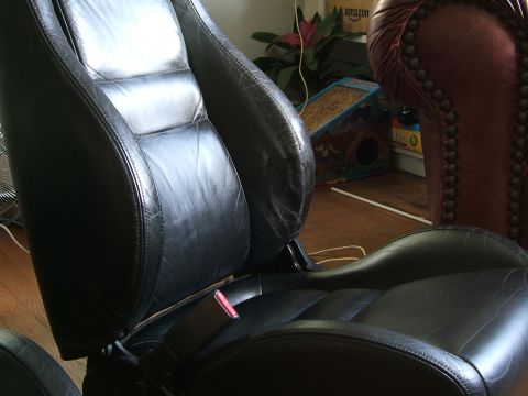 1996 Ford Probe - Close-up of worn black leather car seats, showing stitching and a seatbelt buckle.