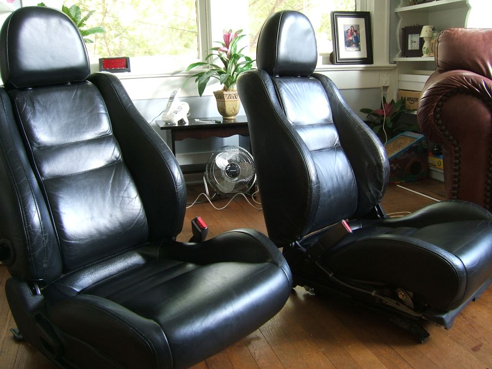Pair of black leather bucket seats removed from a car, sitting on a living room floor