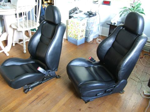 1996 Ford Probe - Two black leather car seats with adjustable bases and red seatbelt buckles are shown indoors.