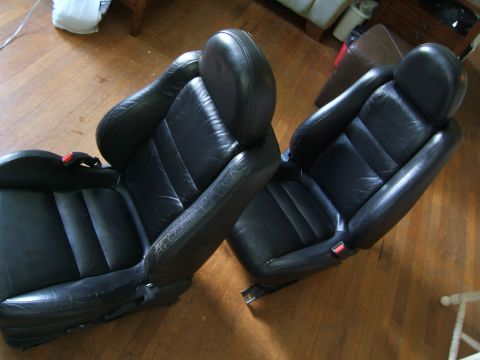 1996 Ford Probe - Two black leather car seats are shown on a wooden floor, likely removed from a vehicle.