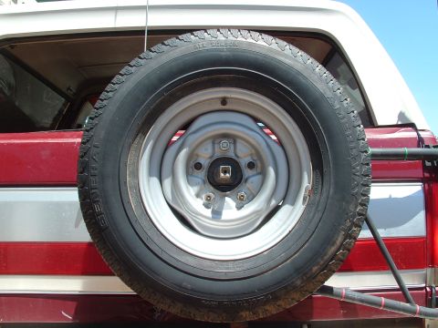 1990 Ford Bronco - Spare tire mounted on the rear of a 1990 Ford Bronco, showing its distinctive red and white paint scheme.