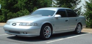 1993 Ford Taurus - Silver Ford Taurus SHO four-door sedan photographed from the front three-quarter angle in a parking lot, showing the body-color grille-less…