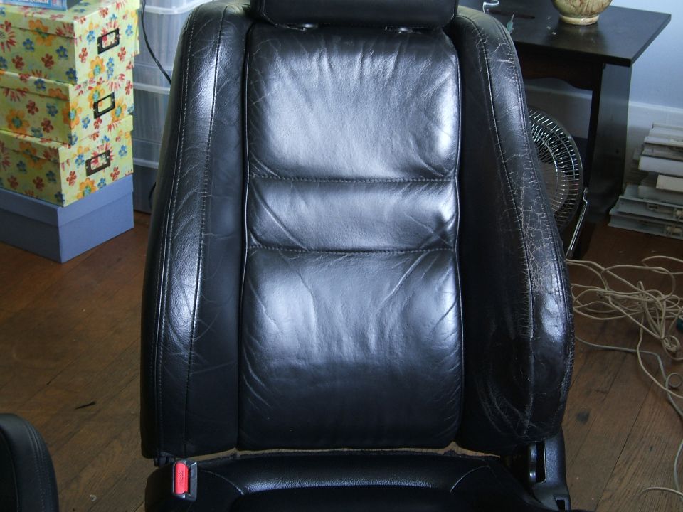 Black leather car seat with visible wear and tear. A red seatbelt buckle is visible
