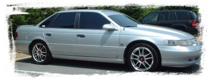 1993 Ford Taurus - Silver Ford Taurus SHO sedan shot from a low front three-quarter angle with a torn-edge white photo border, showing tinted windows, flush b…