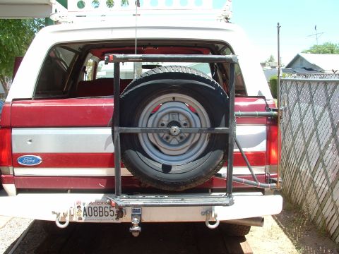 1990 Ford Bronco - The rear of a red and white Ford Bronco, equipped with a spare tire carrier and an Arizona license plate.