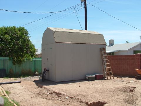 1990 Ford Bronco - A storage shed stands in a dirt yard with a ladder leaning against its side and two coolers nearby.