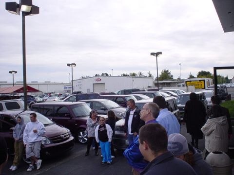 1993 Ford Taurus - A group of people stand in a car lot, with several vehicles visible under an overcast sky.
