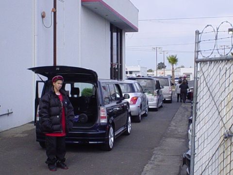 1993 Ford Taurus - A person stands next to a black SUV with its trunk open, in a row of vehicles parked outside a building.