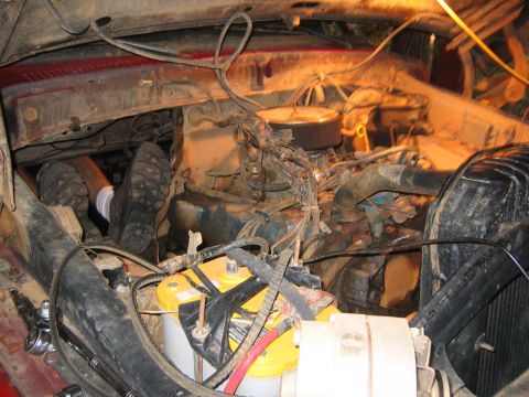 1979 Ford Bronco - A person is working on the engine of a vehicle, with the battery and various engine components visible.