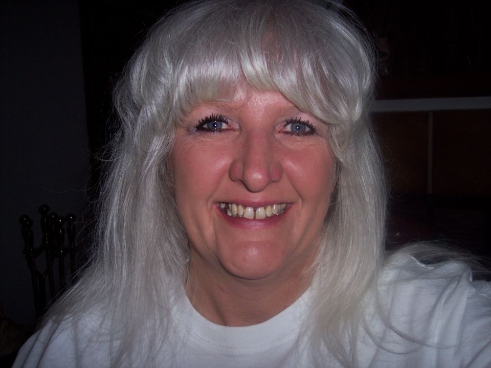 Smiling person with long gray hair in a white t-shirt, indoors