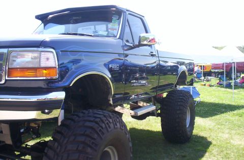 2006 Ford Supercrewzer - This lifted blue pickup truck features flame graphics and F250 badging, suggesting a model from the late 1990s.