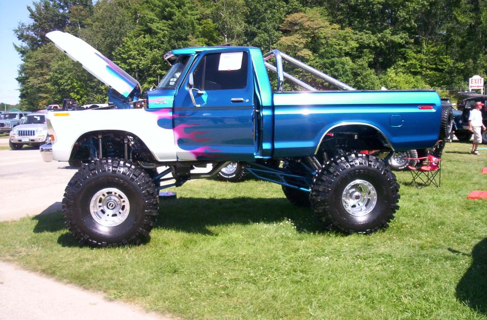Blue and white lifted pickup truck with flame graphics and a roll bar. Hood is open