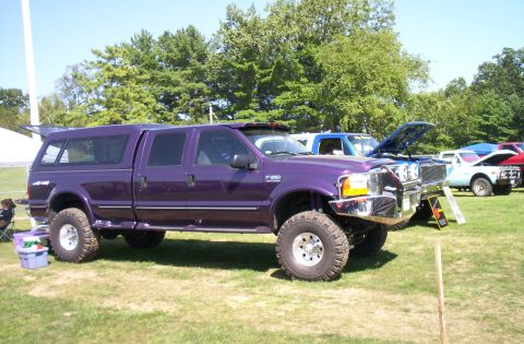 2006 Ford Supercrewzer - A lifted purple 2006 Ford F-250 Super Duty pickup truck with a camper shell is displayed at an outdoor event.