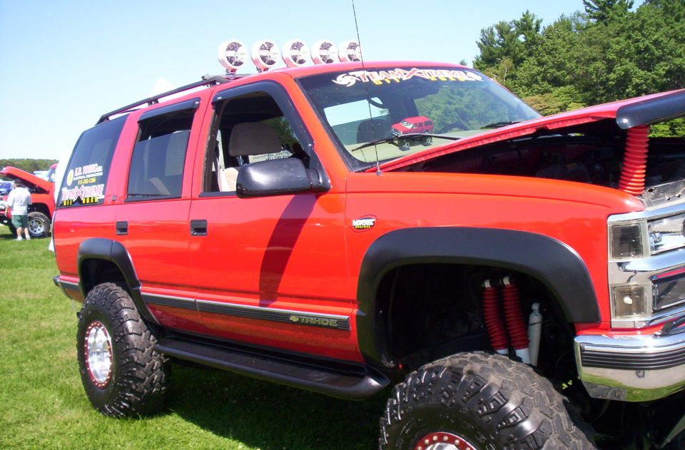 Red lifted SUV with off-road tires, roof lights, and "Tahoe" badge