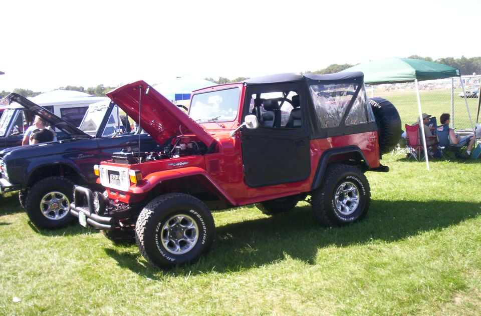 Red Toyota Land Cruiser FJ40 with hood open parked next to a blue Ford Bronco