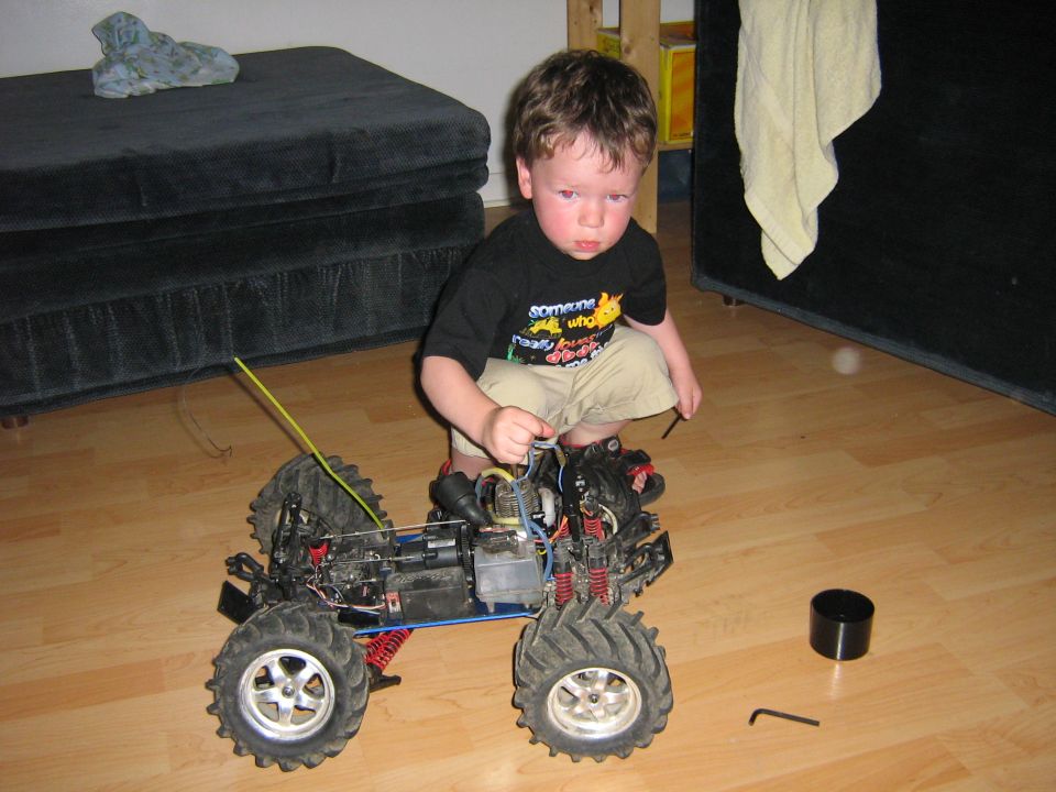 Kid with remote control monster truck on floor. Truck has large tires and exposed engine components