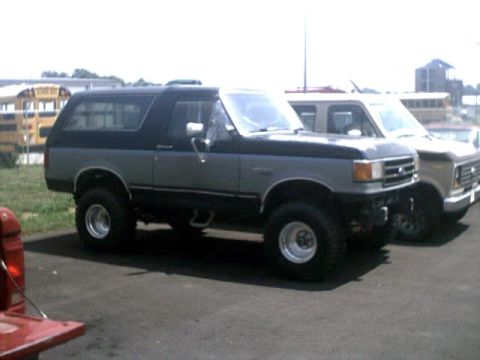 1996 Ford Bronco - A two-tone Ford Bronco is parked next to another truck, with school buses visible in the background.