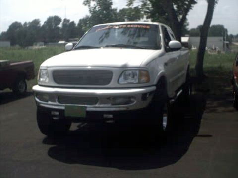 1996 Ford Bronco - A white pickup truck is parked on a paved surface with trees and buildings in the background.